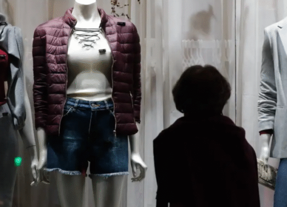 Na imagem, um mulher olhando as roupas na vitrine da loja